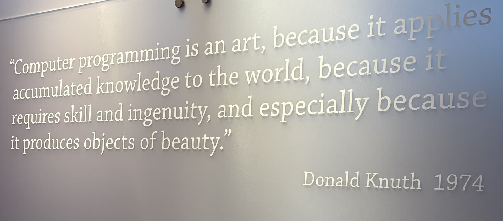 White serif lettering standing off a pale museum wall, angled away from the camera, with Donald Knuth's name and the year 1974 below it to the right.